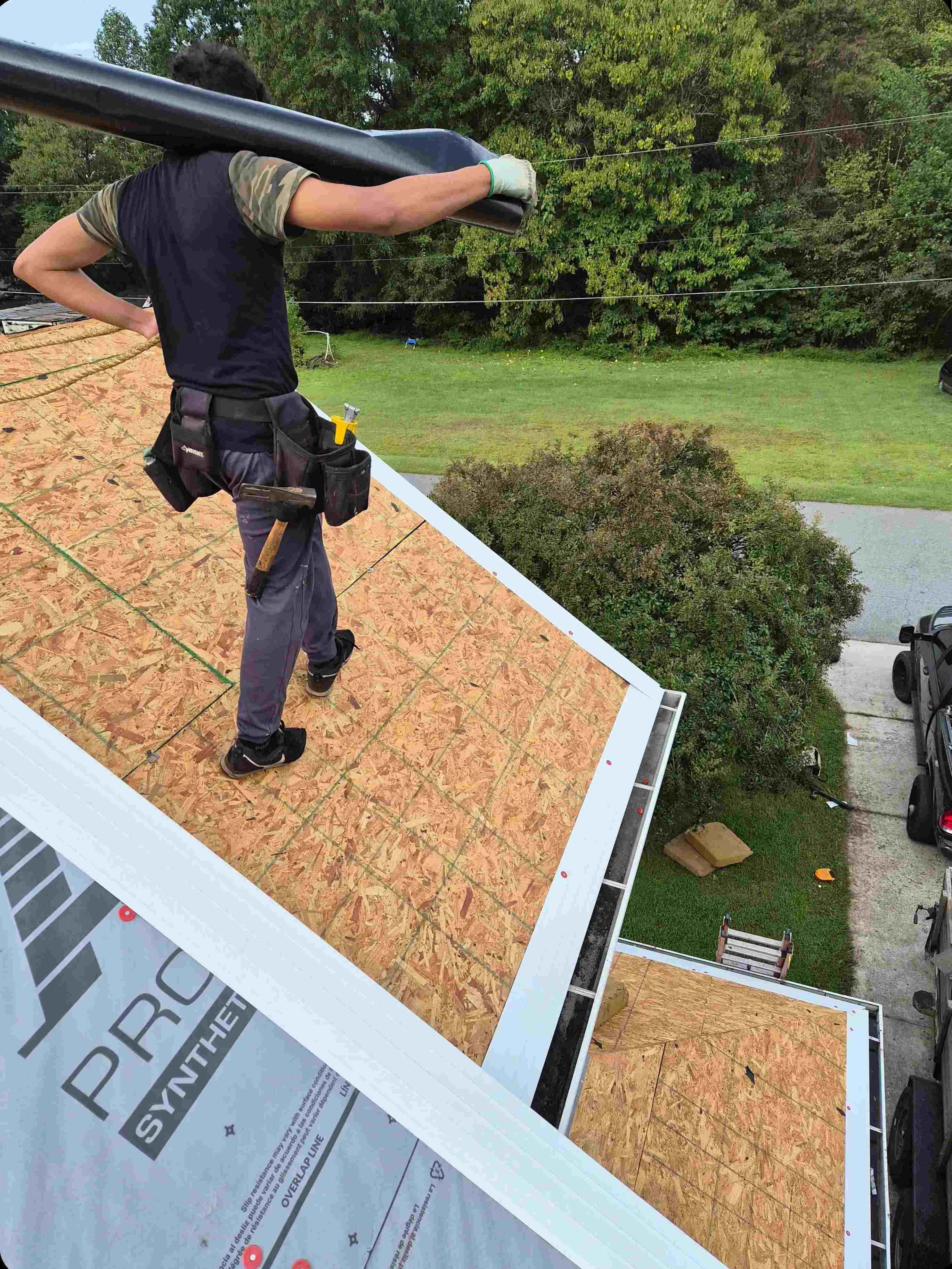 A Blue Hat Roofing crew member carrying underlayment across a new roof deck in Winston-Salem NC